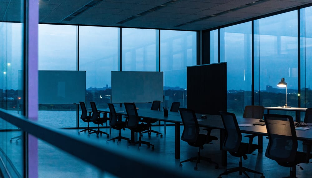 A large glass walled research office in London at dusk, mostly empty, whiteboards wiped clean, one desk lamp still on, c