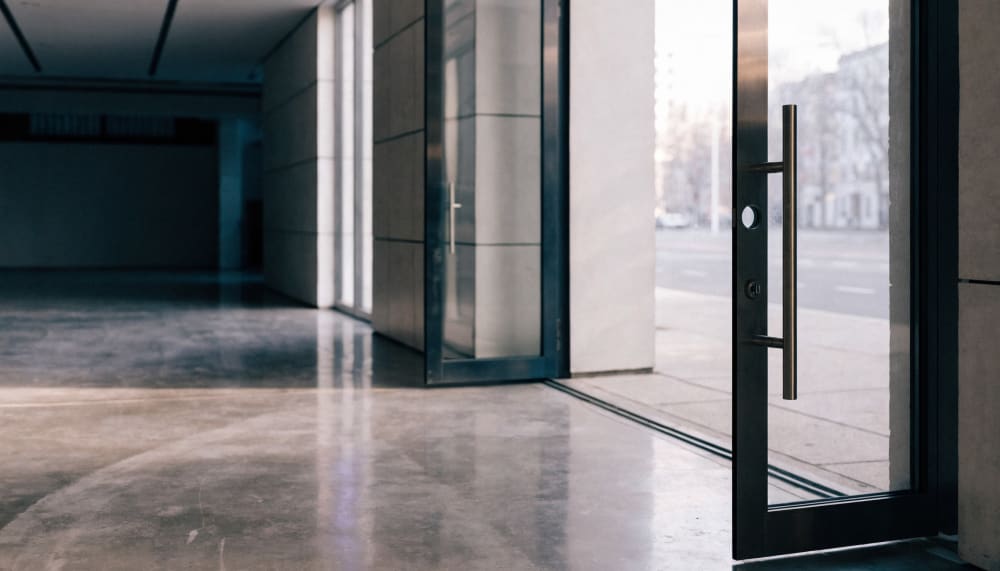 A single glass door standing wide open in an empty modern lobby, the lock hole in the frame visibly empty with no cylind