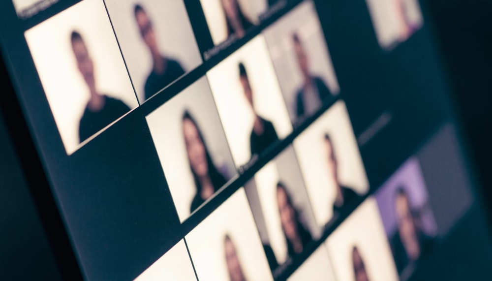 A close-up of a video call grid on a monitor, most participant tiles brightly lit and sharp, one tile at the edge dim an