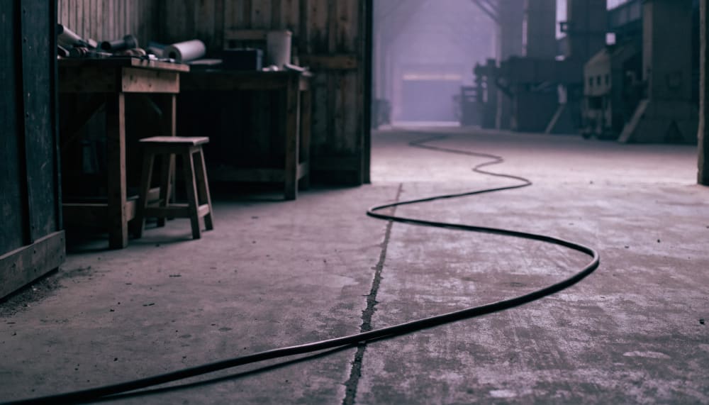 A single thick power cable running from a modest workshop bench across a concrete floor and disappearing through an open
