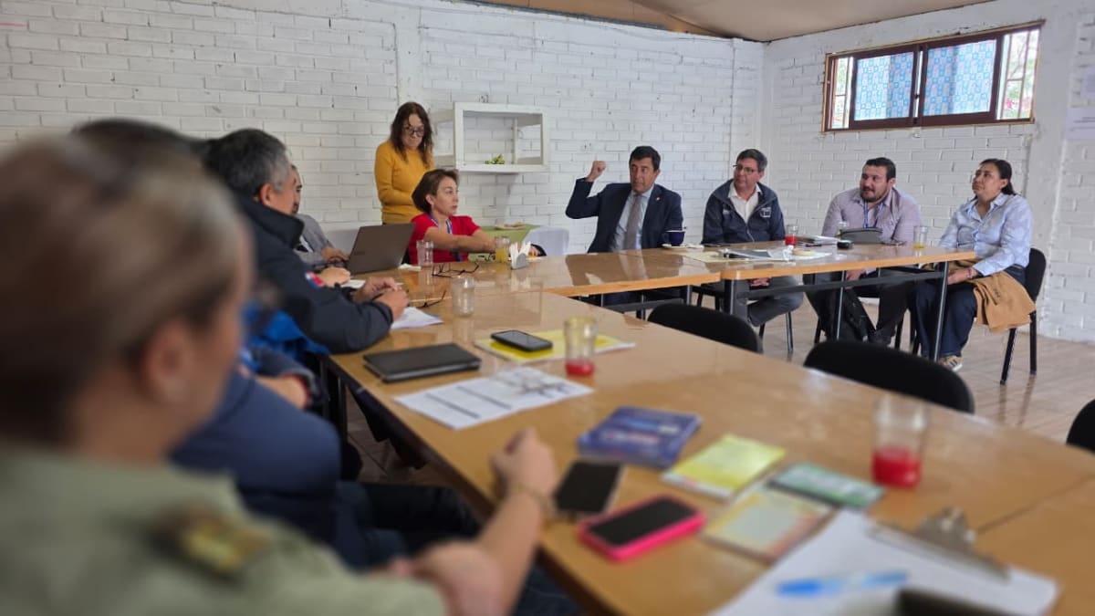 Autoridades y dirigentes sociales reunidos en torno a una mesa en una sala de muros de ladrillo blanco