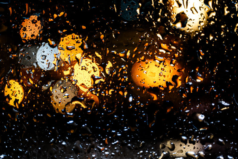 The rain traces invisible paths on the glass, while the city lights dissolve into liquid gold.
