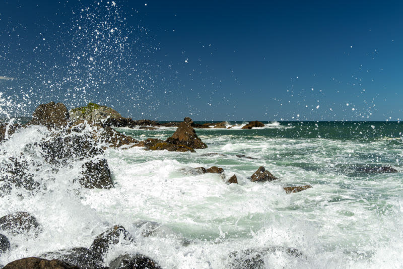 The gentle lapping of waves against moss-covered rocks creates a delicate and mesmerizing visual contrast. A shot that celebrates the beauty in natural details, perfect for prints seeking inspiration and lightness.