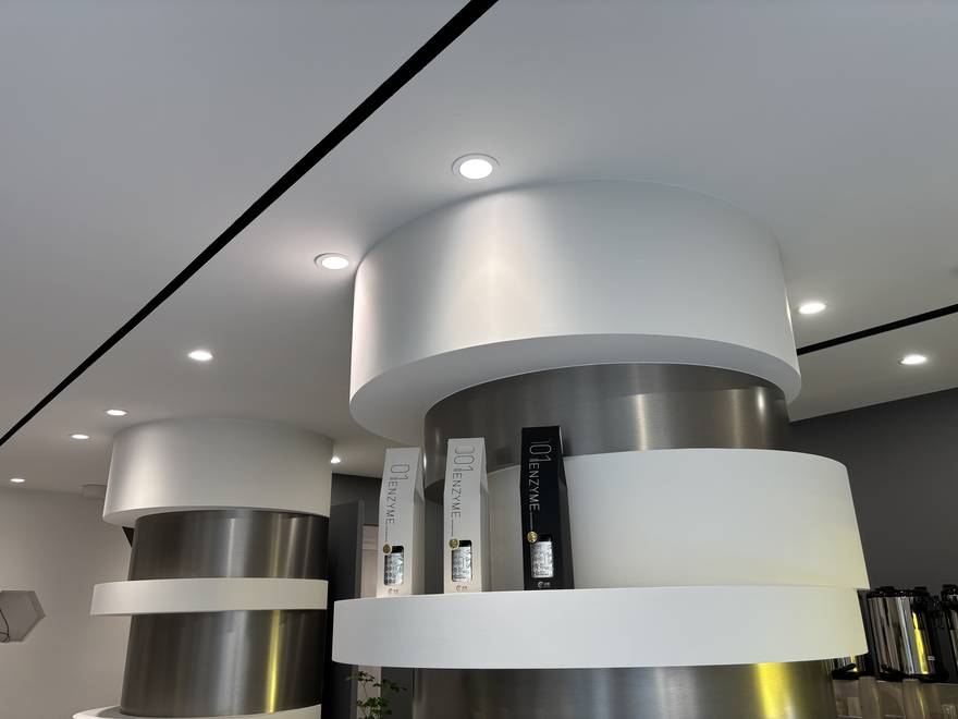 圓柱展示台以不鏽鋼飾帶收邊，搭配六角壁龕陳列 001 ENZYME 酵素產品，延續分子與實驗室語彙