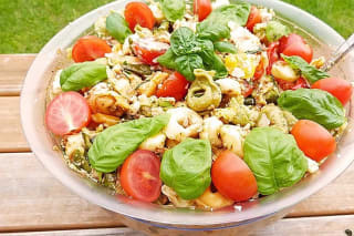 Bunter Tortellini Salat mit grünem Pesto, roten Zwiebelringen und Parmesanstreifen auf einem weißen Teller