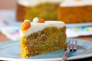 Goldbrauner Rüblikuchen mit glatter Frischkäse‑Zitronen‑Frosting, dekoriert mit geraspelten Karotten.