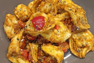 Bunter Tortellinisalat mit rotem Pesto, Kirschtomaten, Feta und Rucola auf einem weißen Teller