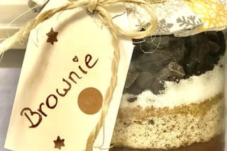 Schichtweise gefülltes Einmachglas mit Brownie-Backmischung, daneben ein frisch gebackener Brownie auf einem Teller