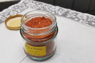 Glas mit selbstgemachter Taco Gewürzmischung neben einer Schüssel Paprikapulver, Chilipulver und Kreuzkümmel