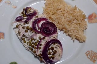 Goldbraun gebackene Putenschnitzel mit hellgelben Zwiebelringen in cremiger Sahnesoße, bestreut mit Parmesan, serviert neben Spaghetti
