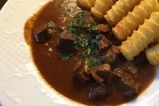 Dampfender Topf mit Gulasch, brauner Schokoladenspiegel und frischer Petersilie