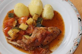 Goldbraun angebratene Kaninchenteile in einem rustikalen Bräter mit Tomaten und Zucchini