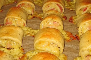 Goldbraun gebackene gefüllte Pizzabrötchen auf Backpapier, Füllung aus Schinken und geschmolzenem Käse sichtbar