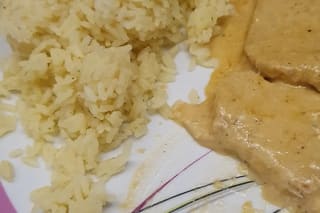 Gebratene Schweine-Minutensteaks mit geschmolzenem Emmentaler, cremiger Sahnesauce und fluffigem Reis, garniert mit grünen Erbsen
