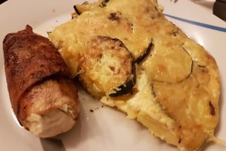 Goldbraune Tortilla mit Zucchini‑ und Kartoffelscheiben, bedeckt mit geschmolzenem Käse und knusprigem Bacon