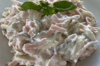 Cremiger Fleischsalat mit goldbraunen Schinkenwurststreifen und frischen Gurkenwürfeln auf einem hellen Teller