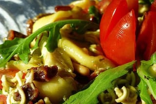 Bunter Tortellini Salat mit grünem Pesto, roten Tomaten und gerösteten Pinienkernen auf einer weißen Schüssel