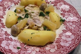 Hähnchenschenkel in cremiger Frikassee mit Karotten, Erbsen und Champignons auf weißem Teller