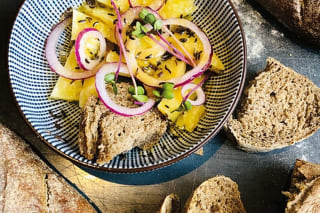 Frisch gebackenes rustikales Bauernbrot mit knuspriger Kruste und goldbrauner Oberfläche, daneben ein Glas Haus-Vinaigrette und dünn geschnittener Deichkäse