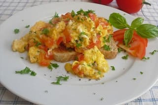 Fluffiges Rührei mit roten Tomatenwürfeln, garniert mit frischen Kräutern, auf einem hellen Teller serviert