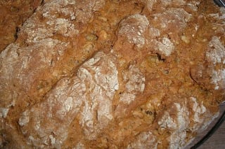 Frisch gebackener Roggenlaib mit goldbrauner Kruste, leicht eingeschnitten, auf einem Holzbrett
