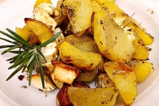 Knusprig gebackene Kartoffelviertel mit goldgelbem Feta und frischen Rosmarinnadeln auf einem Backblech