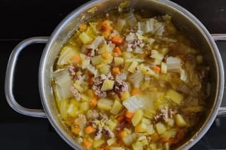 Bunter Topf mit Chinakohl, Hackfleisch, Kartoffelwürfeln und Tomatenstücken, dampfend auf dem Herd