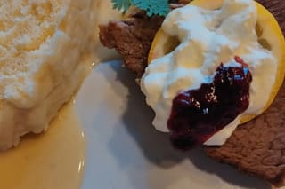 Saftiger Böhmischer Sauerbraten Svickova mit Zitronenscheibe, Preiselbeeren und cremiger Sauce auf weißem Teller