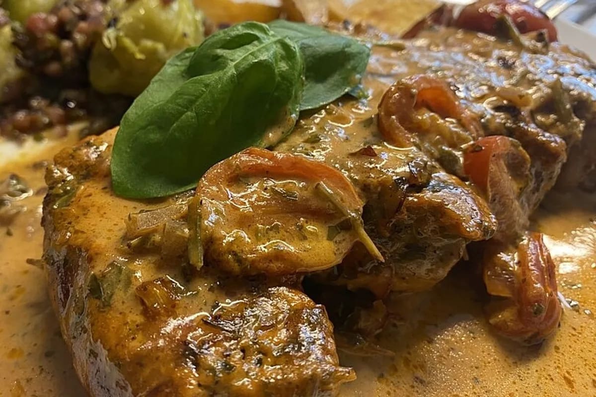 Goldbraun gebratene Schweinefilet-Medaillons in roter Tomaten‑Sahne‑Sauce, garniert mit frischen Basilikumblättern