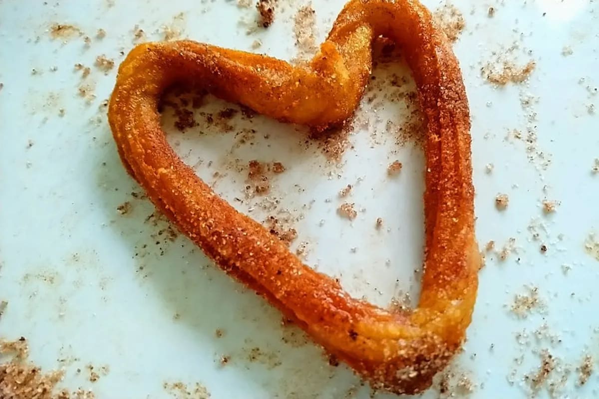 Goldbraune, in Zucker gerollte Churros neben Schokoladensauce auf einem Holzbrett