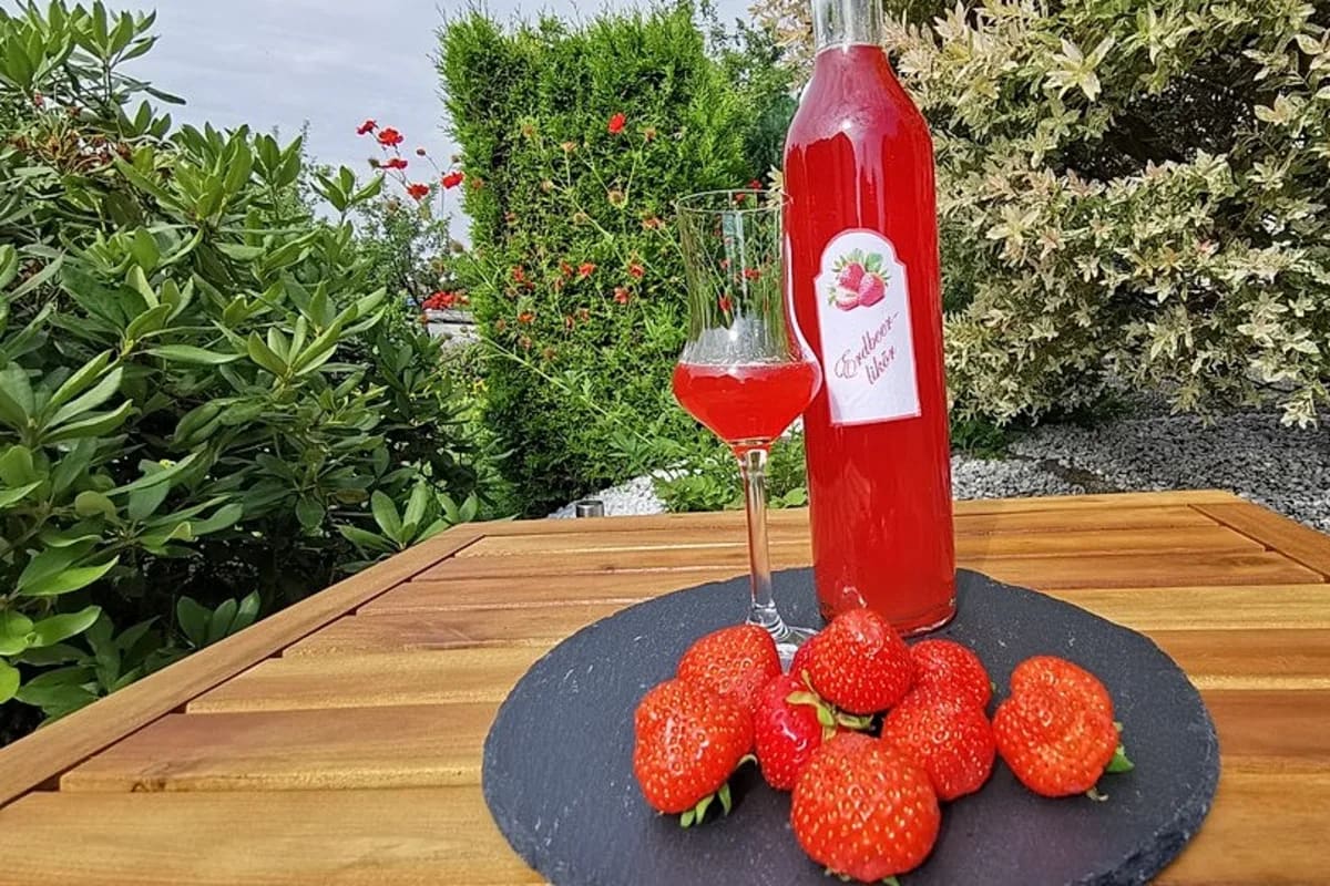 Klare Flasche selbstgemachter Erdbeerlikör mit roter Erdbeerfüllung im Hintergrund