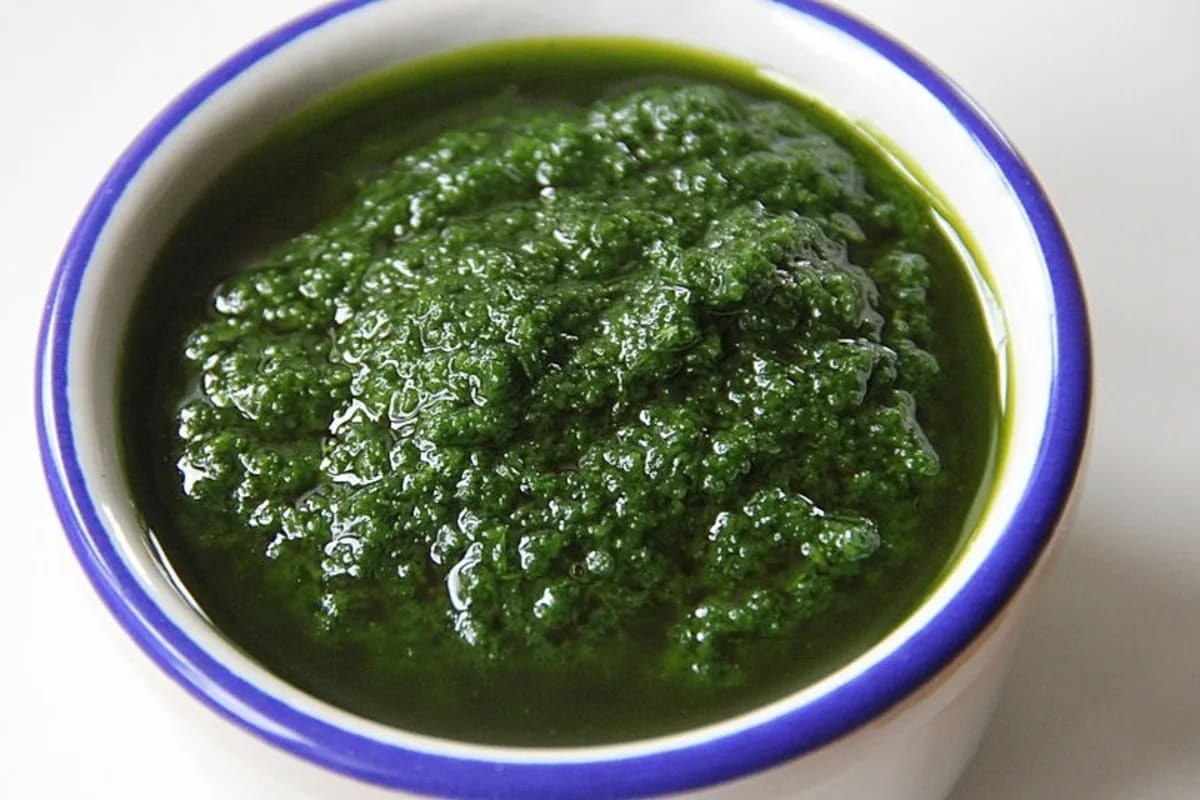 Glas mit grüner Selleriepaste, daneben frische Sellerieblätter und ein kleiner Löffel