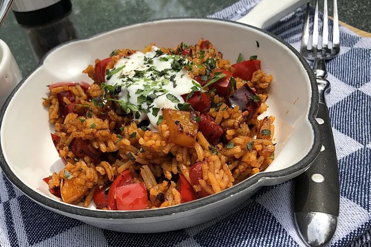 Paprikareis mit Joghurt, garniert mit frischen Kräutern, in einer Pfanne serviert