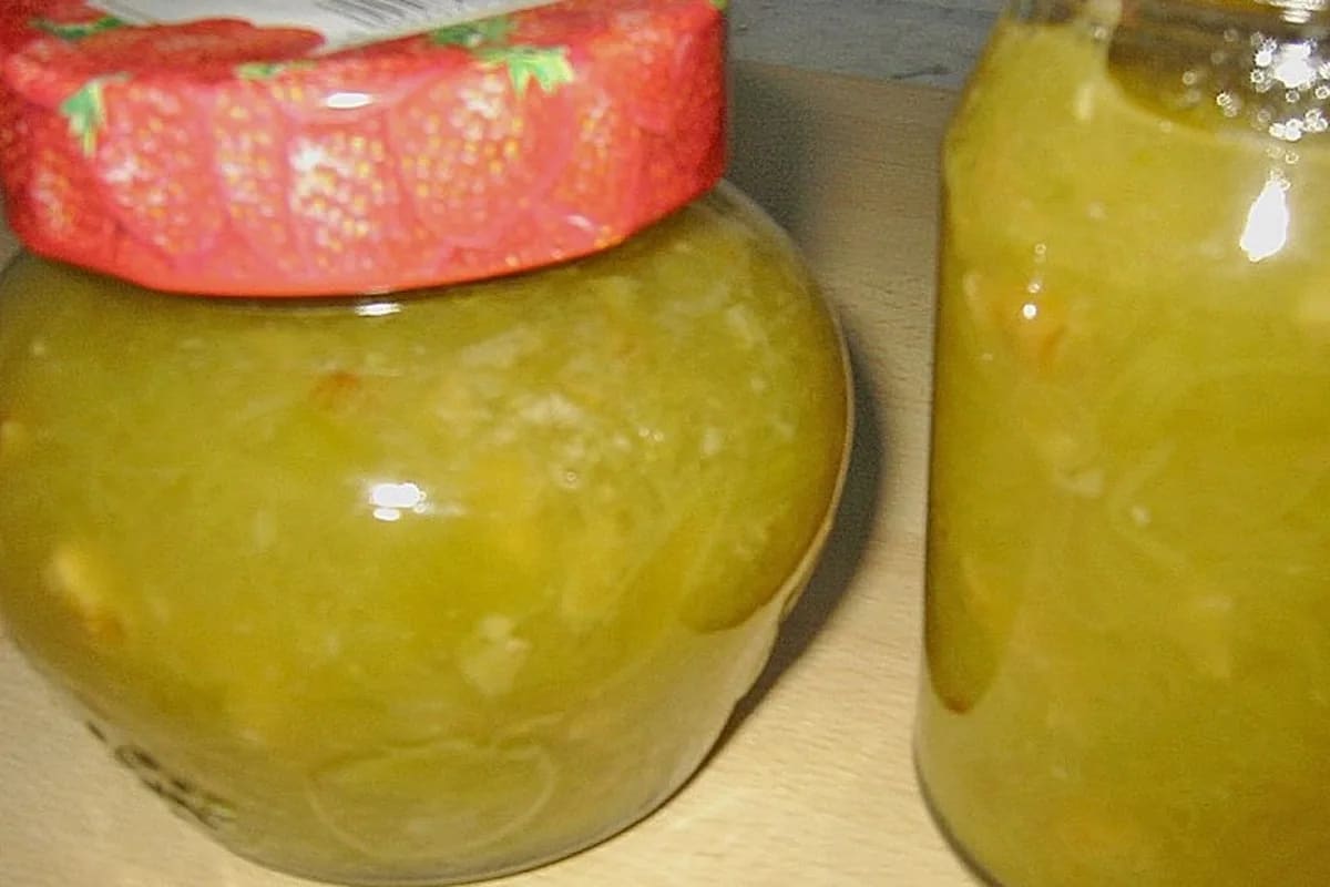 Glas mit ruby-roter Rhabarbermarmelade, ganzen Walnüssen und einem Holzlöffel daneben