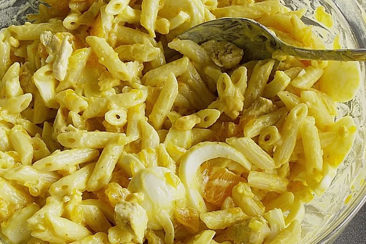 Bunter Curry‑Nudelsalat mit goldenen Nudeln, grünen Paprikastreifen, orangefarbenen Mandarinenstücken und frischen Kräutern auf einem weißen Teller