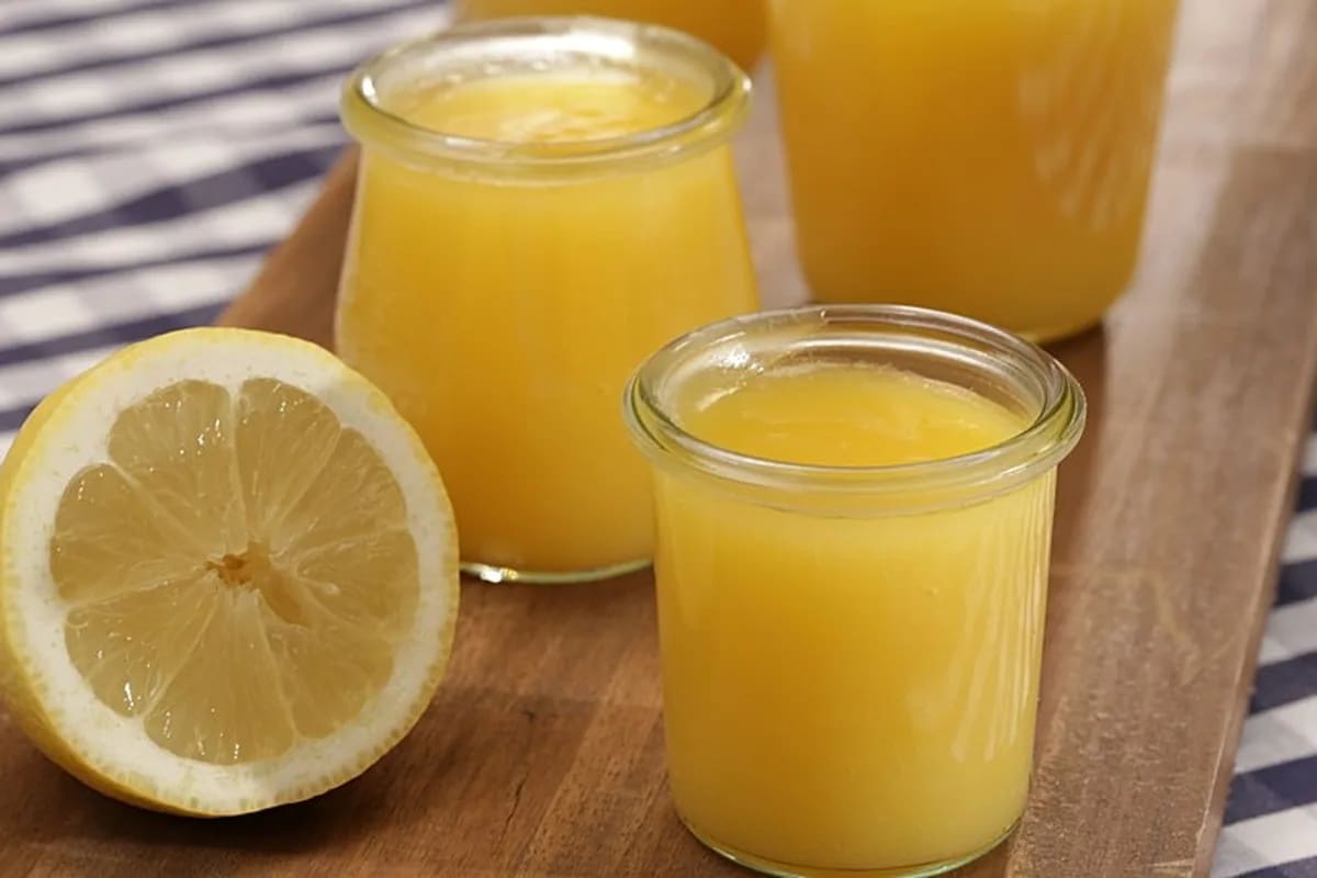 Glas mit goldgelber Lemon Curd, daneben frisch geriebene Zitronenschale und ein Zitronenviertel