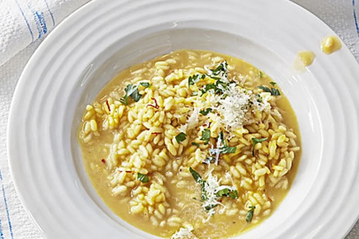 Cremiges Risotto alla Milanese mit goldener Safranfarbe und geriebenem Grana Padano in einem tiefen Teller
