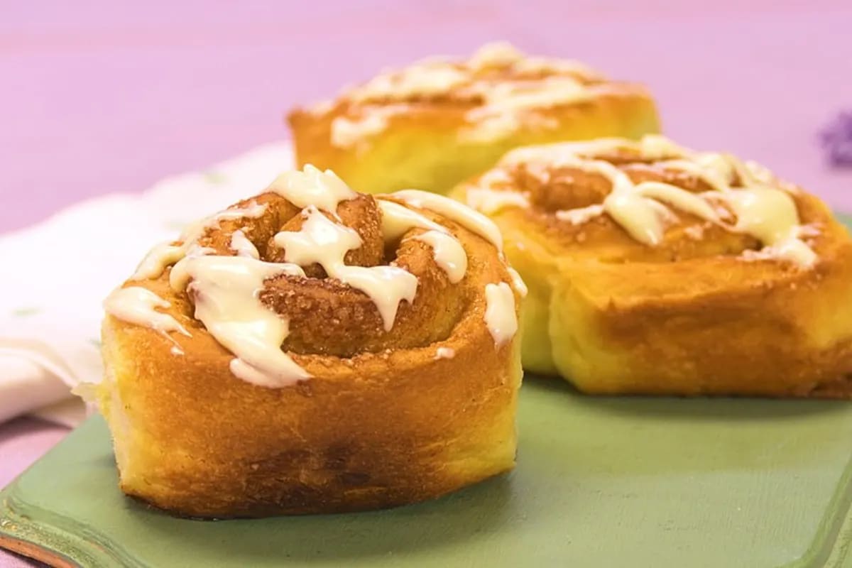 Goldbraune Cinnabon‑Zimtschnecken mit cremiger Glasur auf einem Backblech