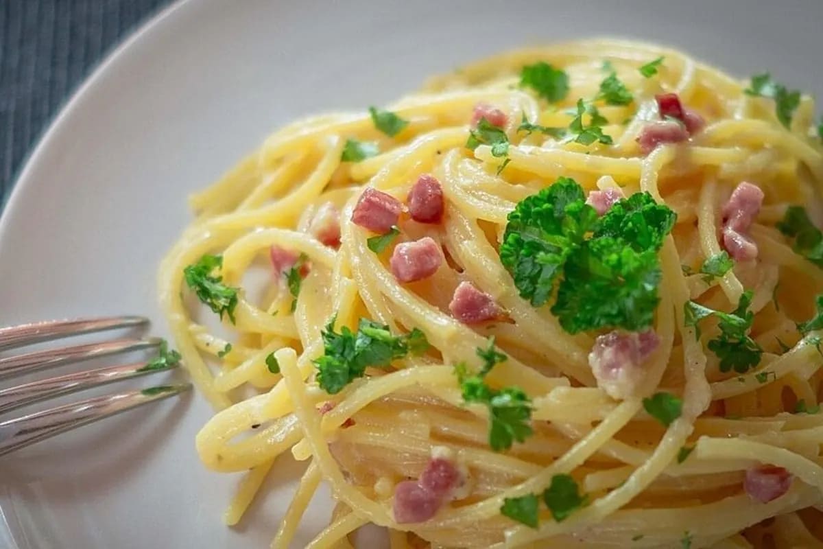 Spaghetti Carbonara in einer Pfanne, cremige Sauce umhüllt die Nudeln, bestreut mit Parmesan und Petersilie