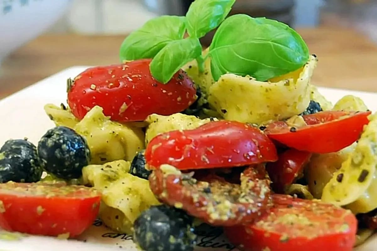 Bunter Tortellini-Pesto-Salat mit Kirschtomaten, Zucchini und Rucola auf einem Holzbrett