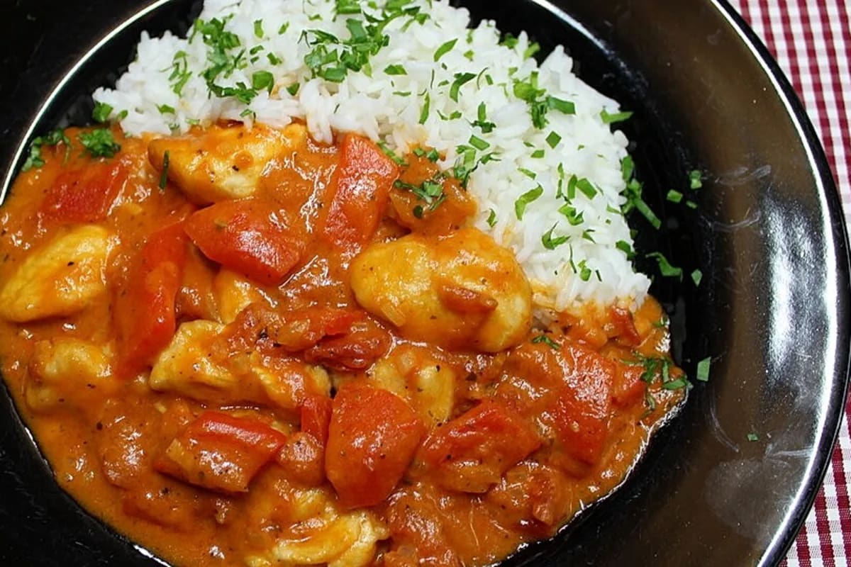 Goldbraun gebratene Hähnchenstücke in cremiger Paprika‑Sahne‑Soße, angerichtet neben fluffigem Reis
