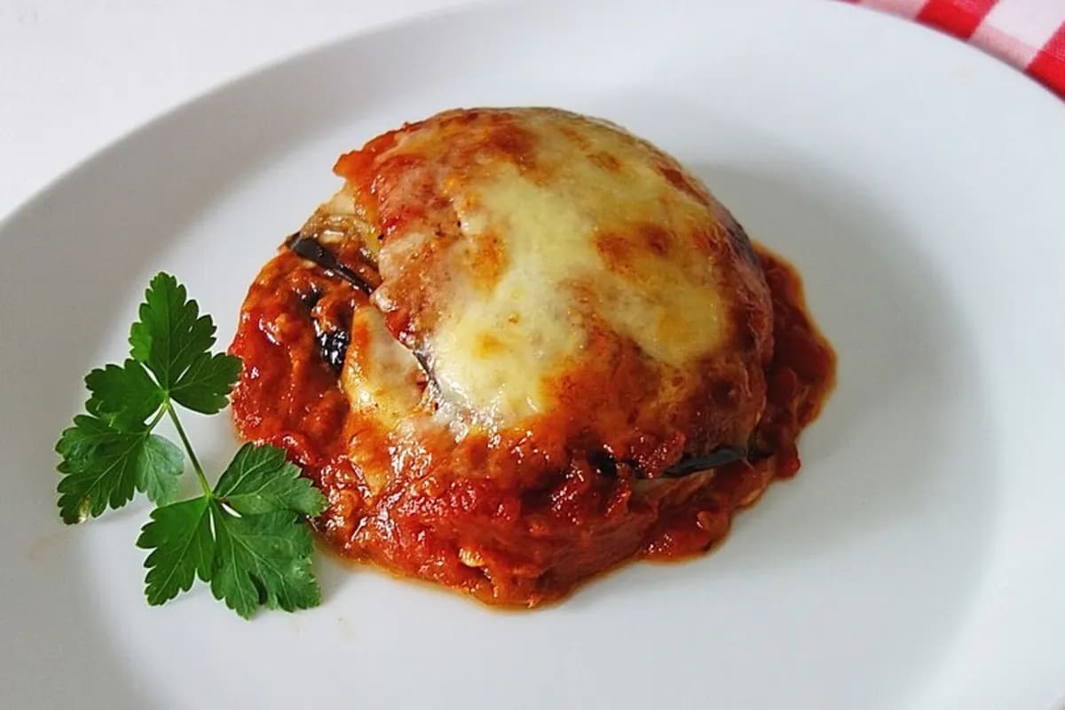 Schichtweise angeordnete Auberginen, Tomatensauce, geschmolzener Mozzarella und Parmesan in einer Auflaufform, goldbraun überbacken