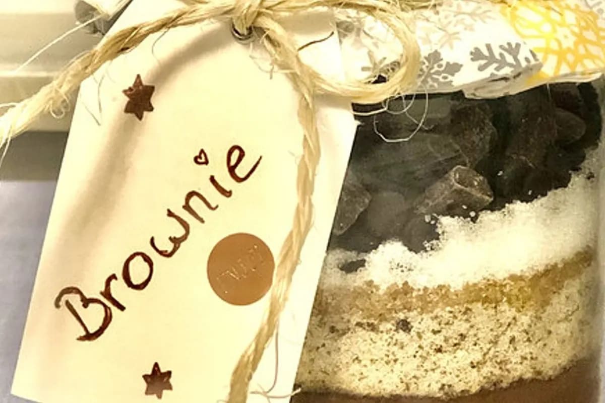 Schichtweise gefülltes Einmachglas mit Brownie-Backmischung, daneben ein frisch gebackener Brownie auf einem Teller