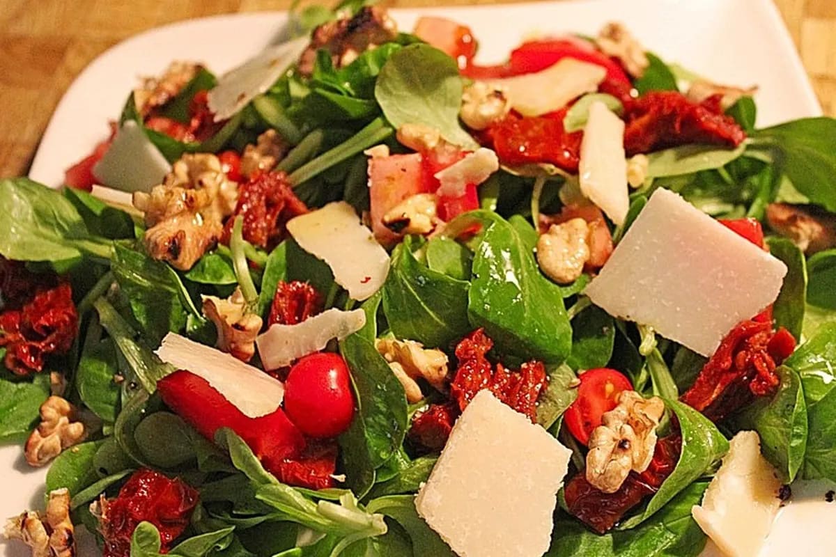 Frischer italienischer Salat mit Rucola, Tomaten, Walnüssen und geriebenem Parmesan auf einer weißen Schale