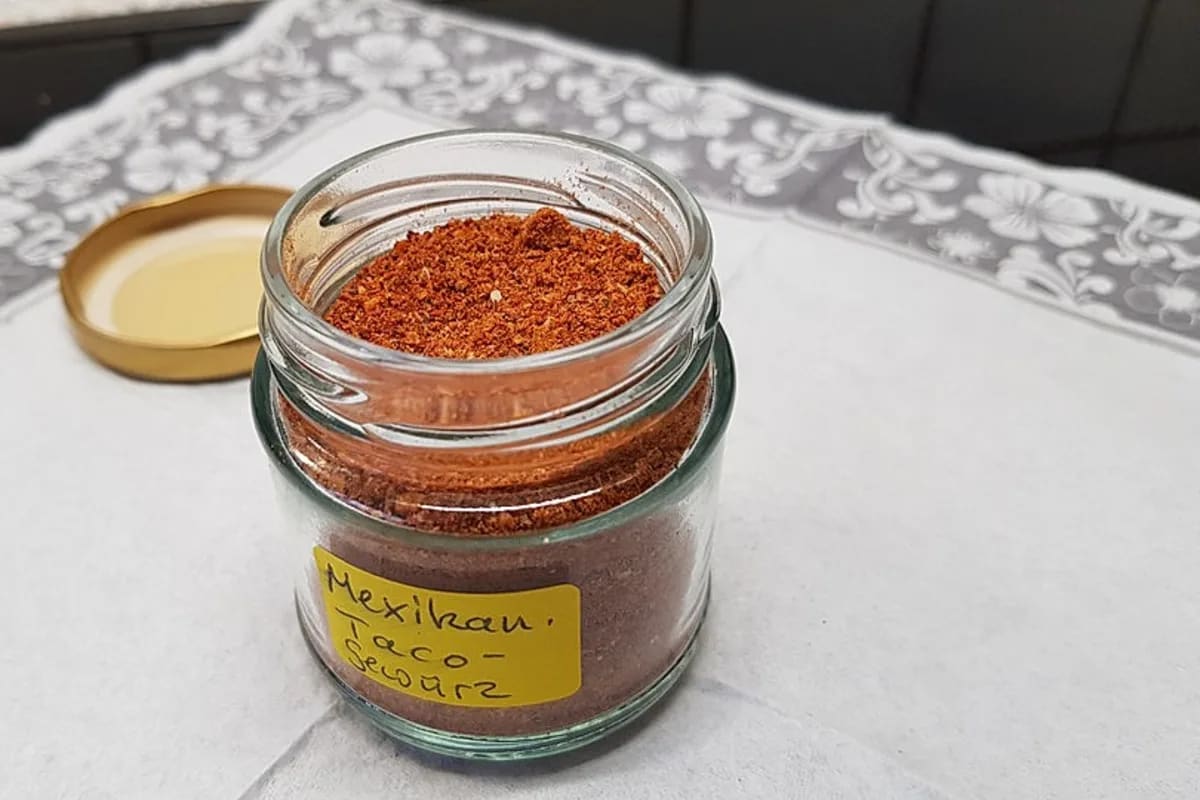 Glas mit selbstgemachter Taco Gewürzmischung neben einer Schüssel Paprikapulver, Chilipulver und Kreuzkümmel