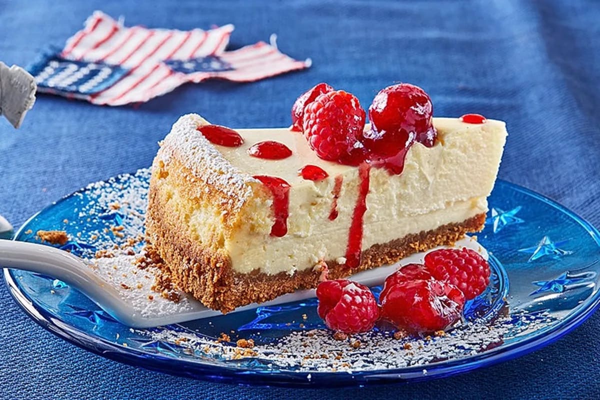 Ein Stück des ultra-cremigen New York Cheesecakes auf einem weißen Teller, garniert mit Zitronenzesten