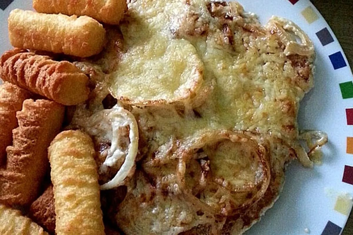 Knusprig überbackenes Schnitzel mit goldenen Zwiebelringen, cremiger Sauce und geschmolzenem Käse