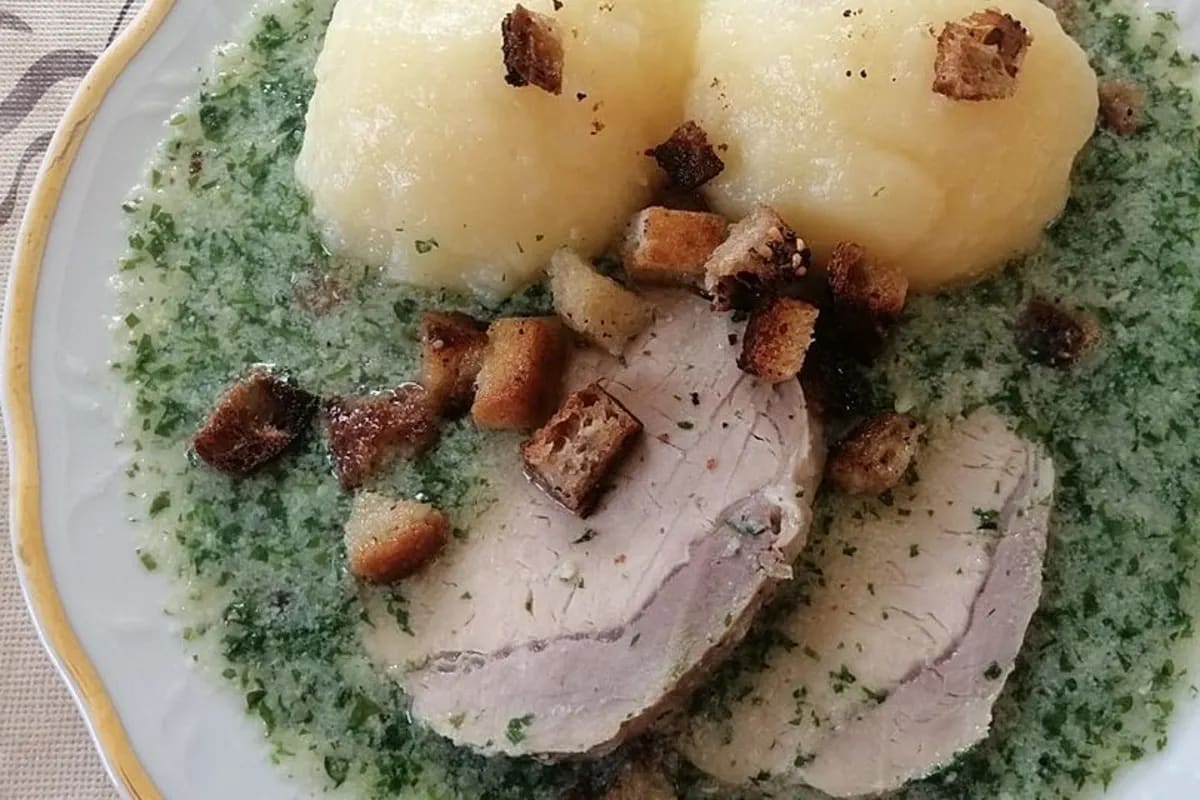 Omas Petersiliensoße mit zarten Fleischscheiben, fluffigen Kartoffelklößen und goldbraunen Croûtons auf einem rustikalen Teller