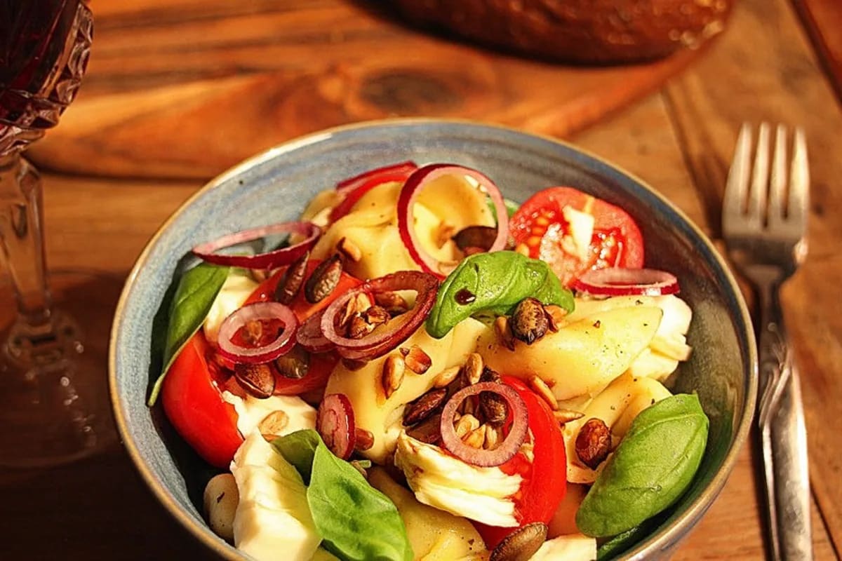 Bunter Tortellini-Salat mit rotem Pesto, halbierten Cocktailtomaten, Mozzarella‑Würfeln und schwarzen Oliven auf weißem Teller