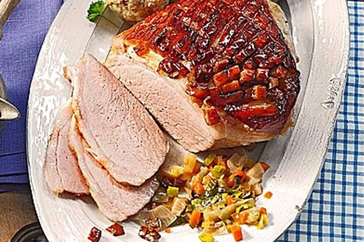 Goldbraun gebratener bayerischer Krustenbraten mit knuspriger Schwarte, dunkler Biersauce und daneben liegenden Semmelknödeln